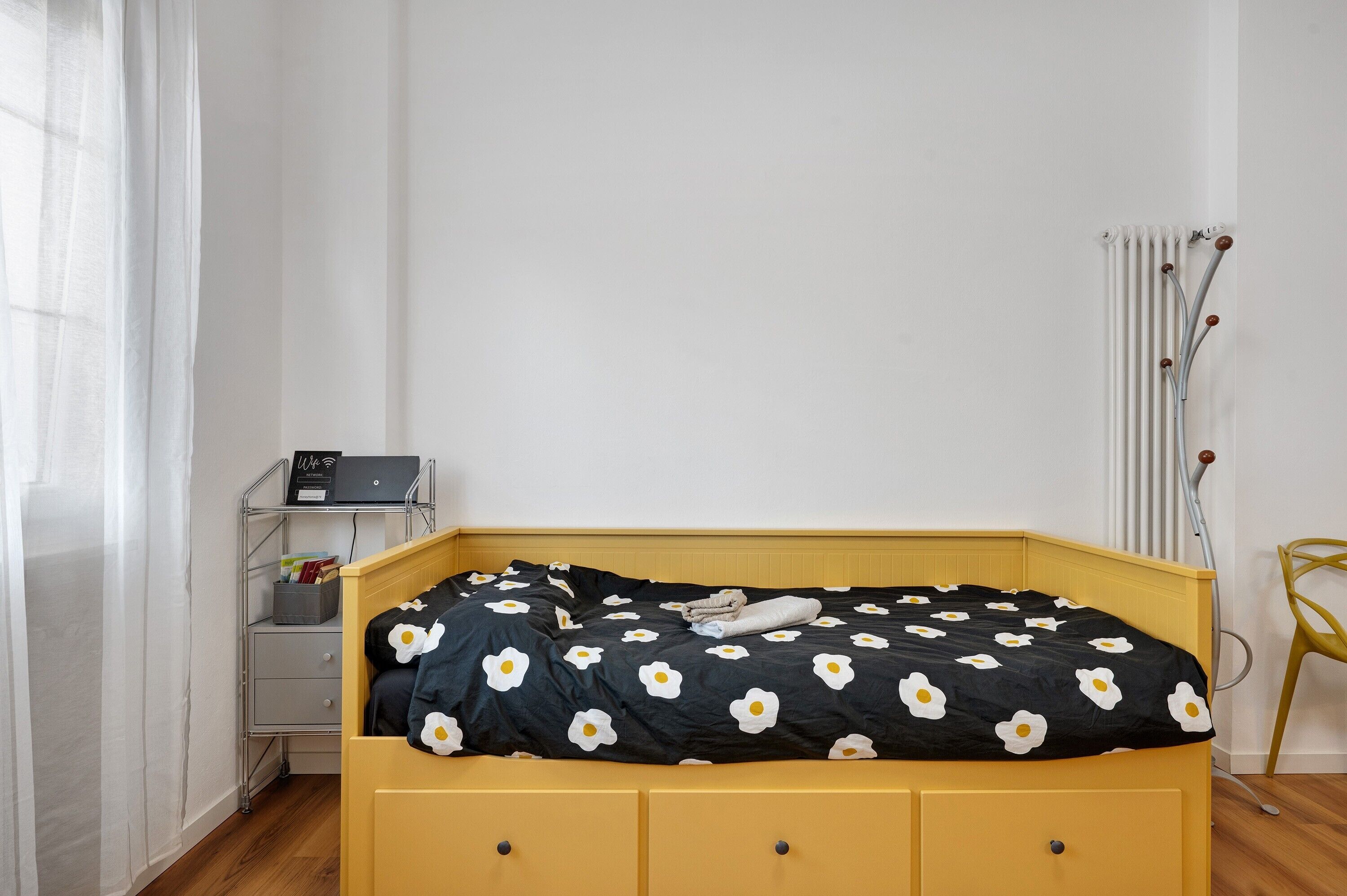 Ein Bett mit schwarz-weiß gestreifter Bettdecke, ein Nachttisch mit Lampe und ein Heizkörper.