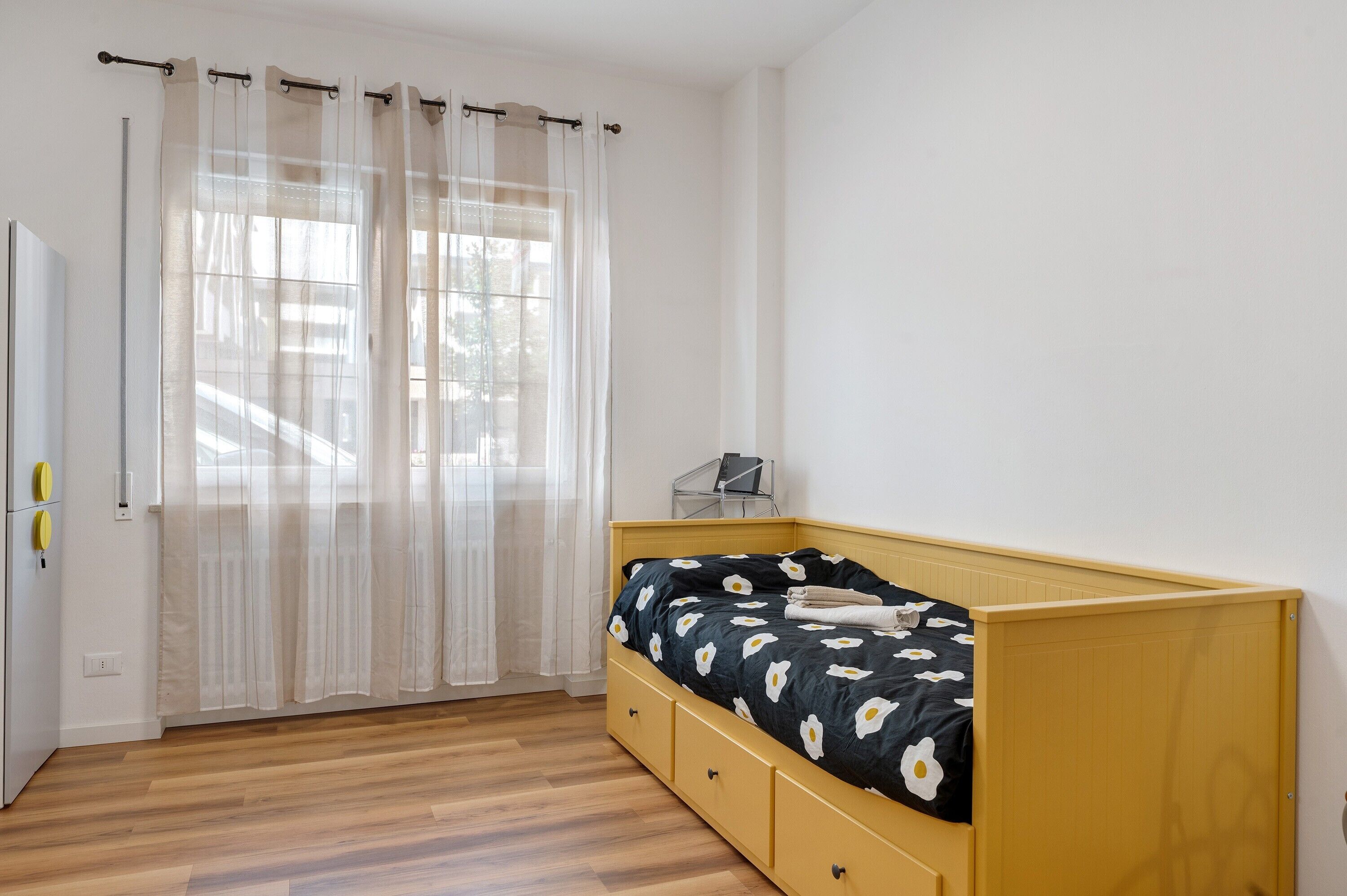 Une chambre à coucher avec un lit, un bureau et une fenêtre ornée de rideaux légers.