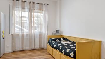 Une chambre à coucher avec un lit, un bureau et une fenêtre ornée de rideaux légers.