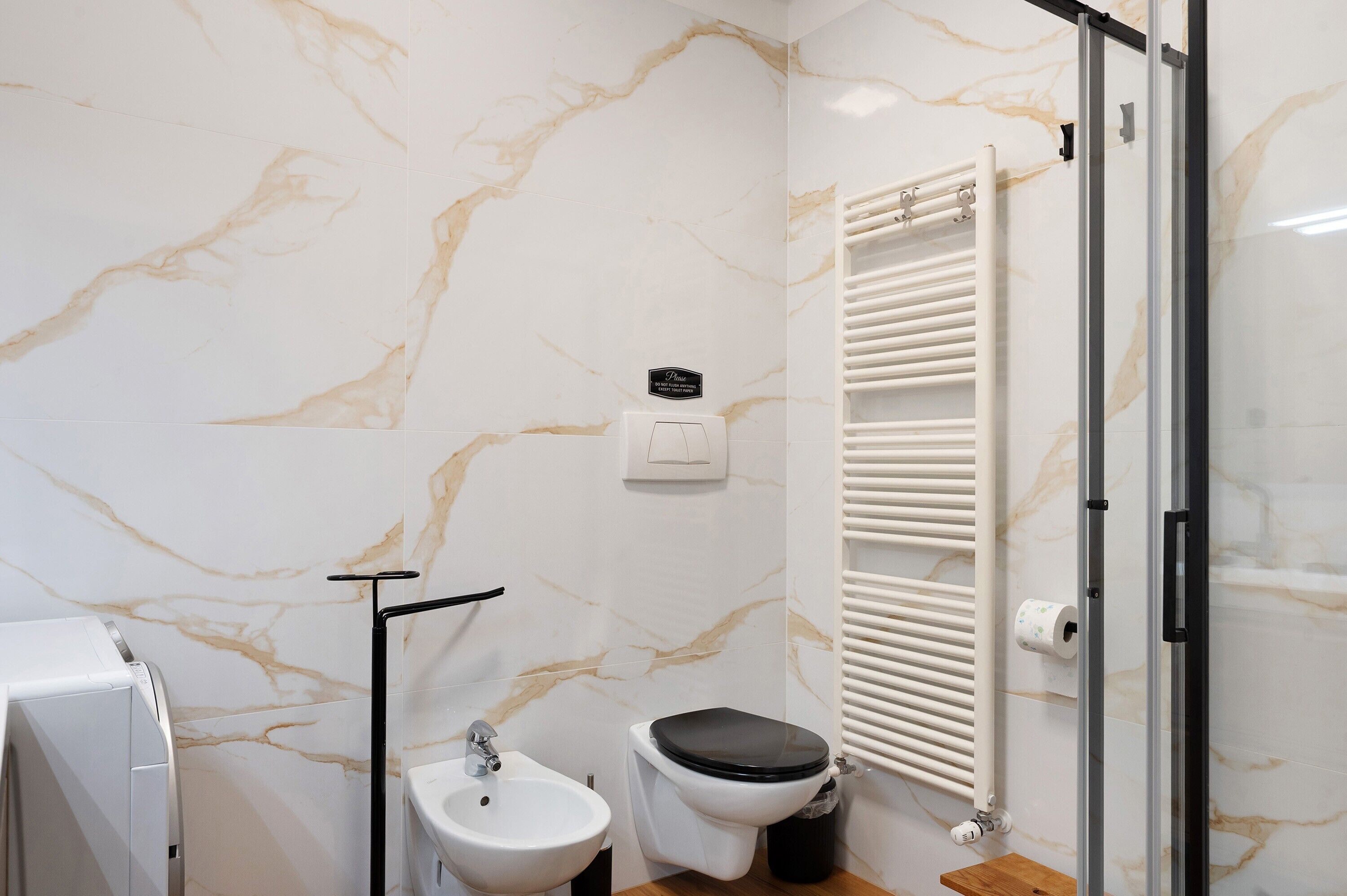 A bathroom with a marble wall, a toilet, a sink, a towel rack, and a glass shower enclosure.