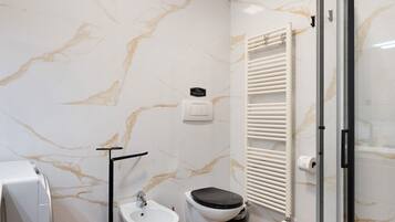 A bathroom with a marble wall, a toilet, a sink, a towel rack, and a glass shower enclosure.