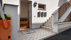 Une entrée d’immeuble d’habitation avec un sol carrelé, une porte en bois, une petite fenêtre et un escalier.