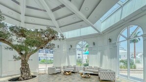 A spacious room with a large potted tree, white upholstered sofas, and large windows offering views of the outdoors. - Luxury 1BR Lagoon View Arjan near Miracle Garden by Green Sky Holiday Homes (Dubai)