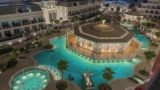 A luxurious hotel with a central courtyard featuring a swimming pool, palm trees, and a fountain. - Luxury 1BR Lagoon View Arjan near Miracle Garden by Green Sky Holiday Homes (Dubai)