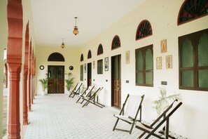 A corridor with arched windows and doors, patterned floor tiles, and a row of chairs. - kushal niwas (Bassi)