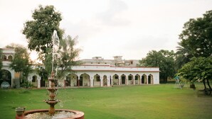 A courtyard with a fountain, a white building with arches, and a swing set. - kushal niwas (Bassi)