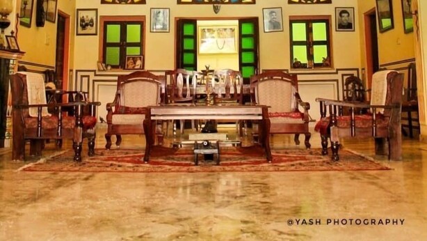 A spacious room with a large chandelier, multiple framed pictures, and a central table with chairs. - kushal niwas (Bassi)