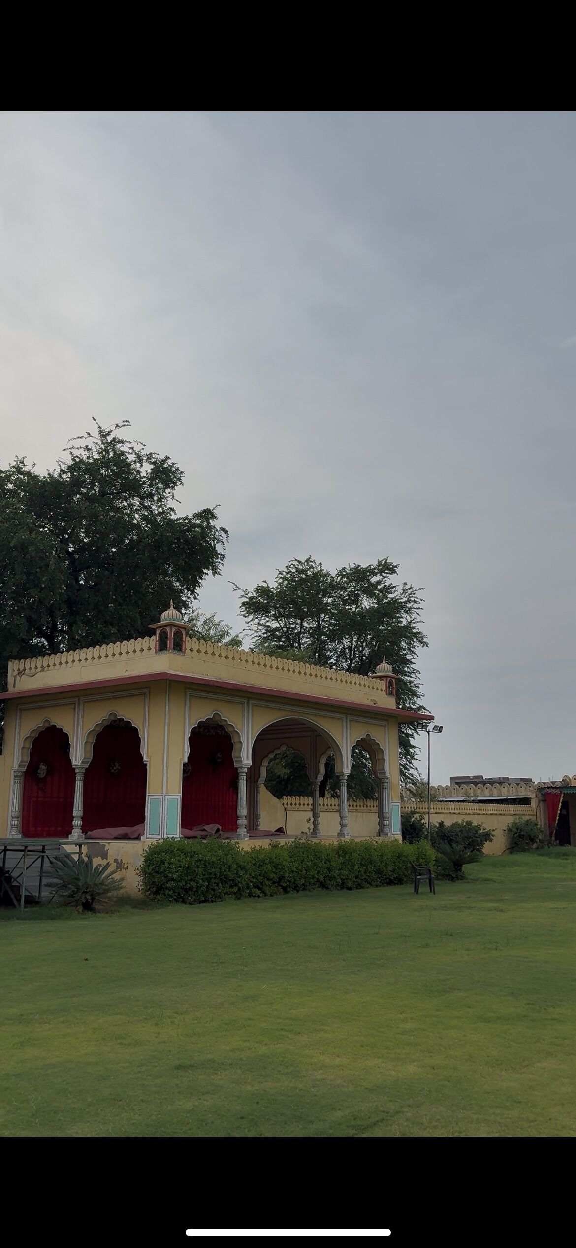 A traditional building with multiple arches and a domed roof, surrounded by greenery.