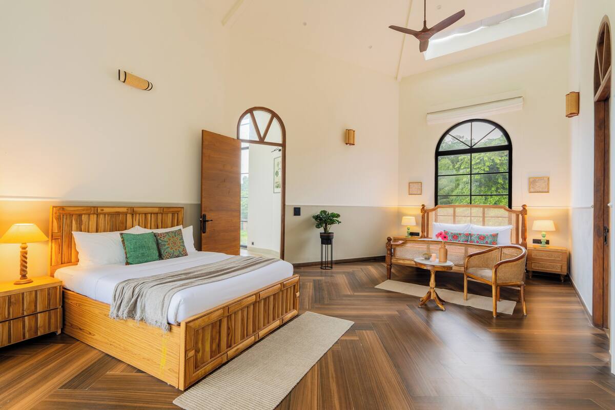 Un dormitorio amplio con una cama grande, cabecera de madera y vistas a la vegetación a través de una ventana.