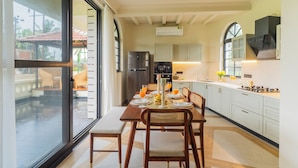 A modern kitchen with a dining area, featuring a large window, ceiling fan, and built-in appliances. - Water Edge by Akama Homes- 4Bhk Luxe (Arpora)