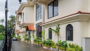 A row of white buildings with red-tiled roofs, large windows, and potted plants along the sidewalk. - Water Edge by Akama Homes- 4Bhk Luxe (Arpora)