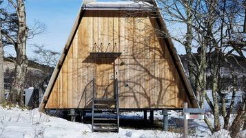 A wooden cabin with a metal staircase leading to a door, surrounded by snow and trees.