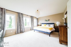 Ein Schlafzimmer mit einem großen Bett, zwei Nachttischen, einem Schminktisch und einer Kandelaber.