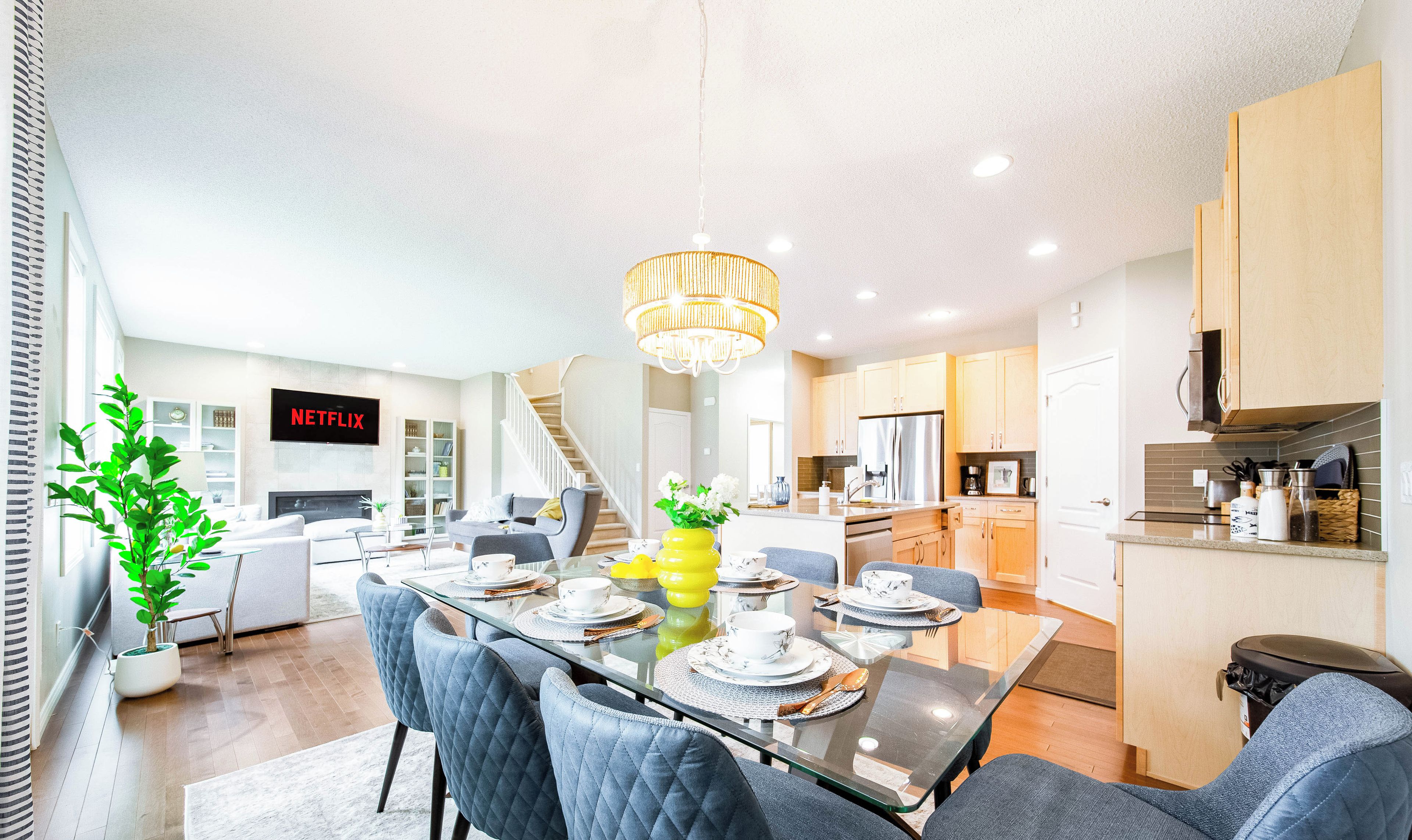 A modern kitchen with a built-in oven, a dining area with a glass table, and a staircase leading to an upper level.
