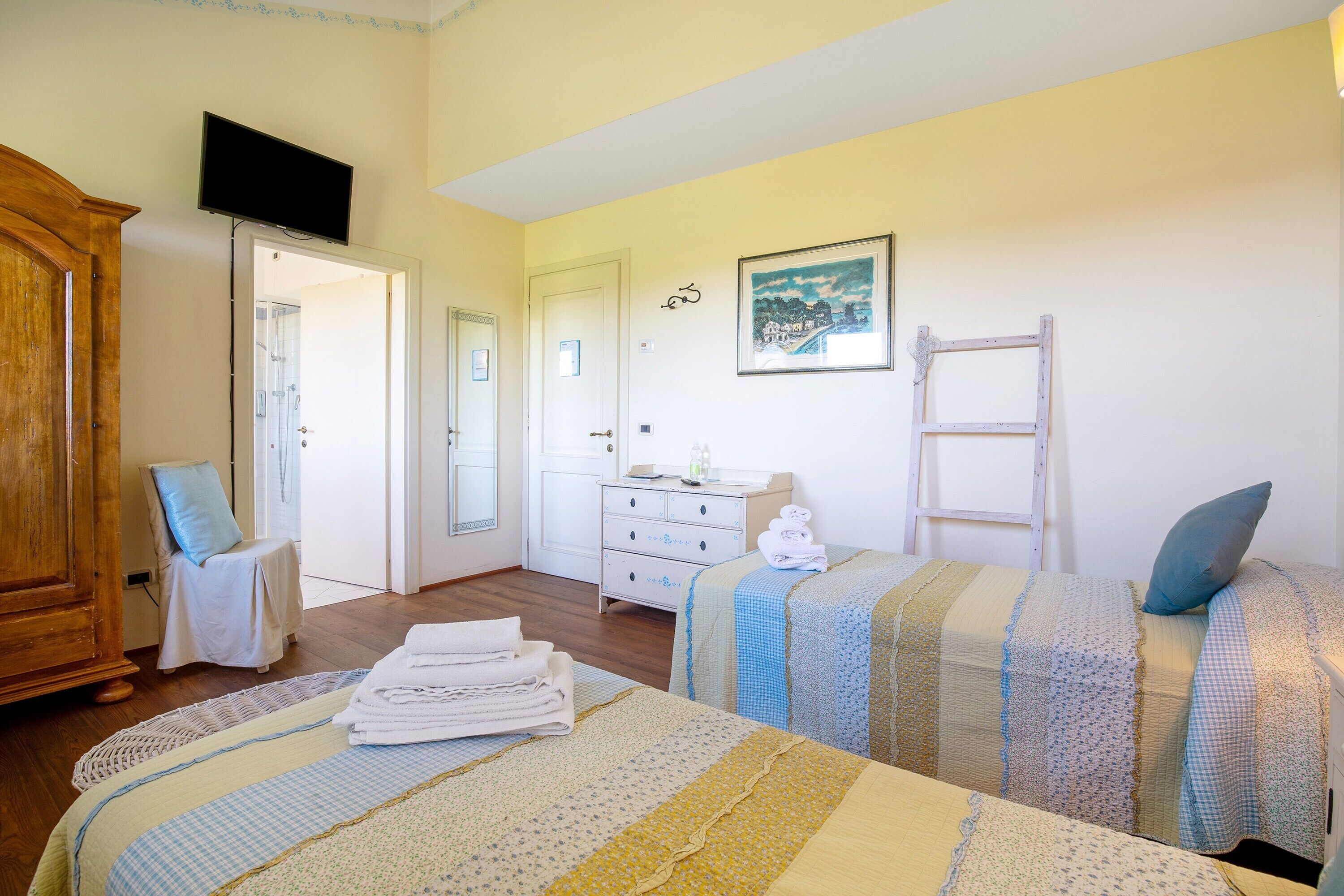 Une chambre avec deux lits, une armoire en bois, un téléviseur, une commode blanche et un tableau accroché au mur.