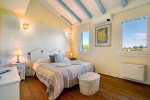 Una camera da letto con un letto, lampade sui comodini, un poggiapiedi in vimini, una finestra con vista e un termosifone.