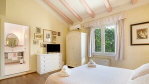 A bedroom with a bed, a dresser, a television, a wardrobe, a window with curtains, and framed pictures on the wall. - Room 'Rosa' with Shared Garden, Wi-Fi and Air Conditioning (Mirano)