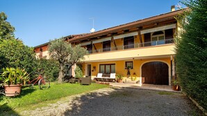 A two-story building with a balcony, a gravel driveway, and outdoor furniture. - Room 'Rosa' with Shared Garden, Wi-Fi and Air Conditioning (Mirano)