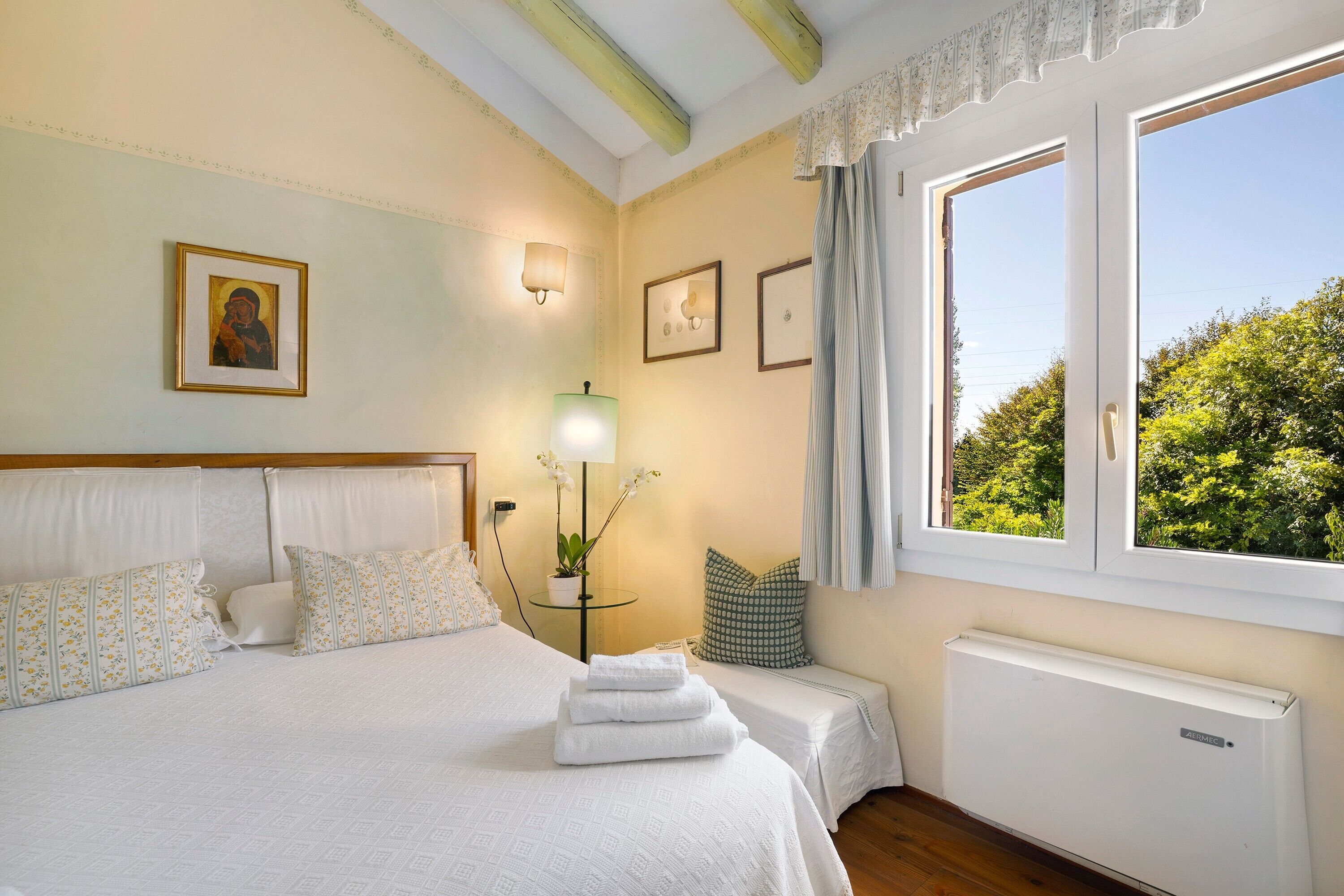 A bedroom with a bed, two bedside tables, a window with a view, and a radiator.