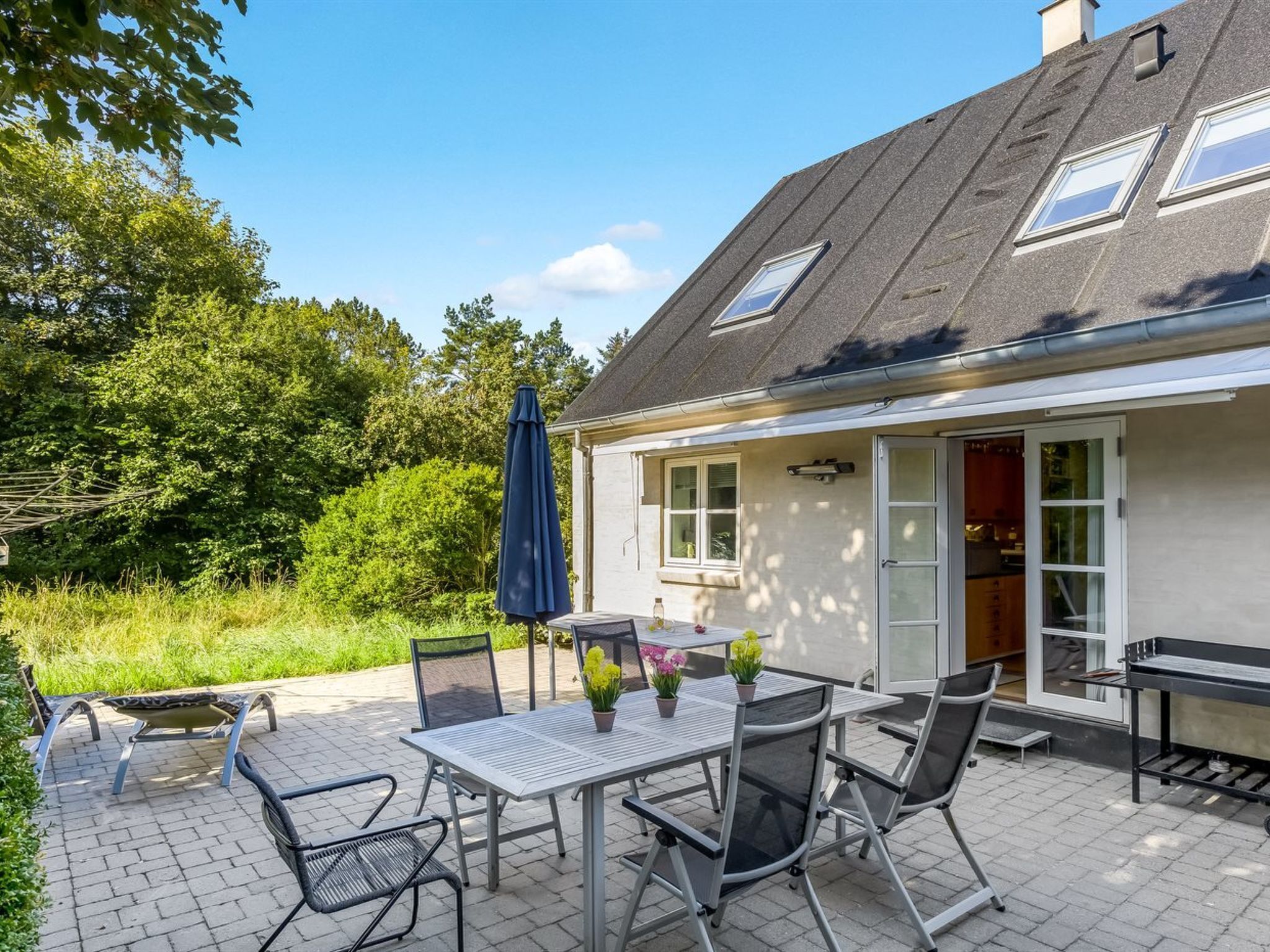 Une terrasse avec une table et des chaises, un parasol bleu et un coin jardin.