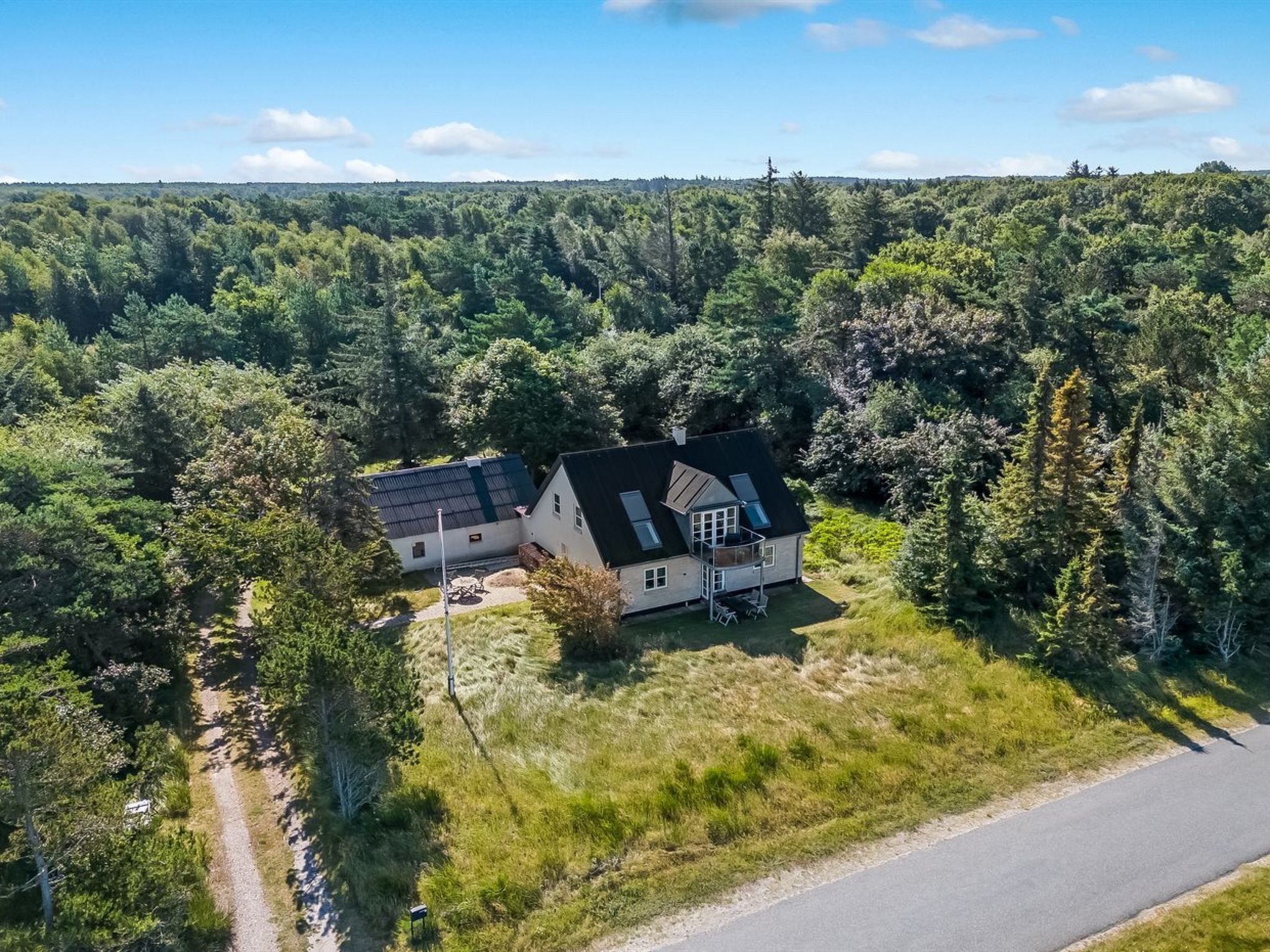 A house surrounded by dense forest, with a paved road nearby.