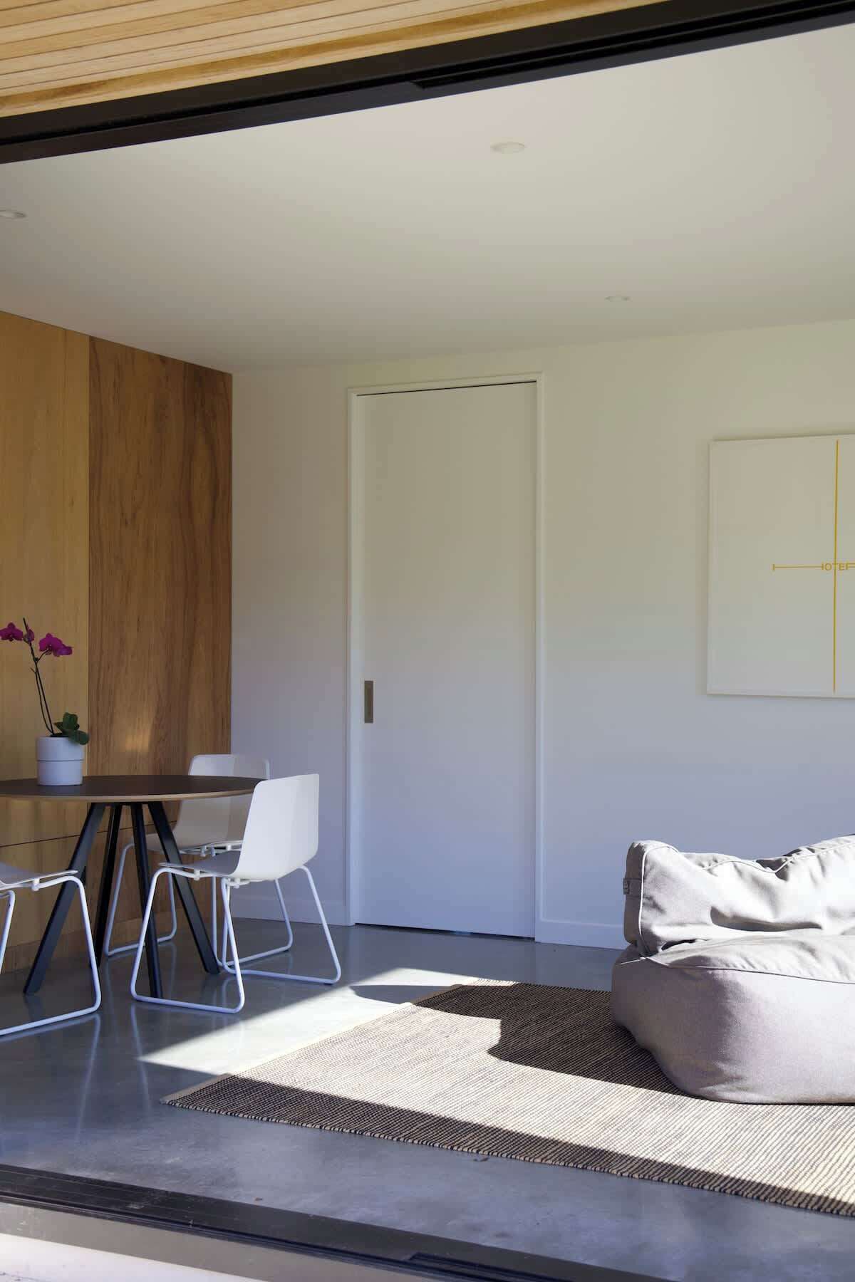 A modern living room with a sofa, a dining table with chairs, and a wooden accent wall.