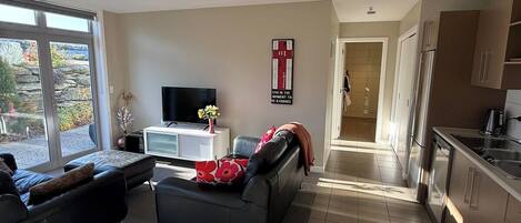 A modern living room with a sofa, a TV, and a kitchen area with cabinets and a refrigerator.
