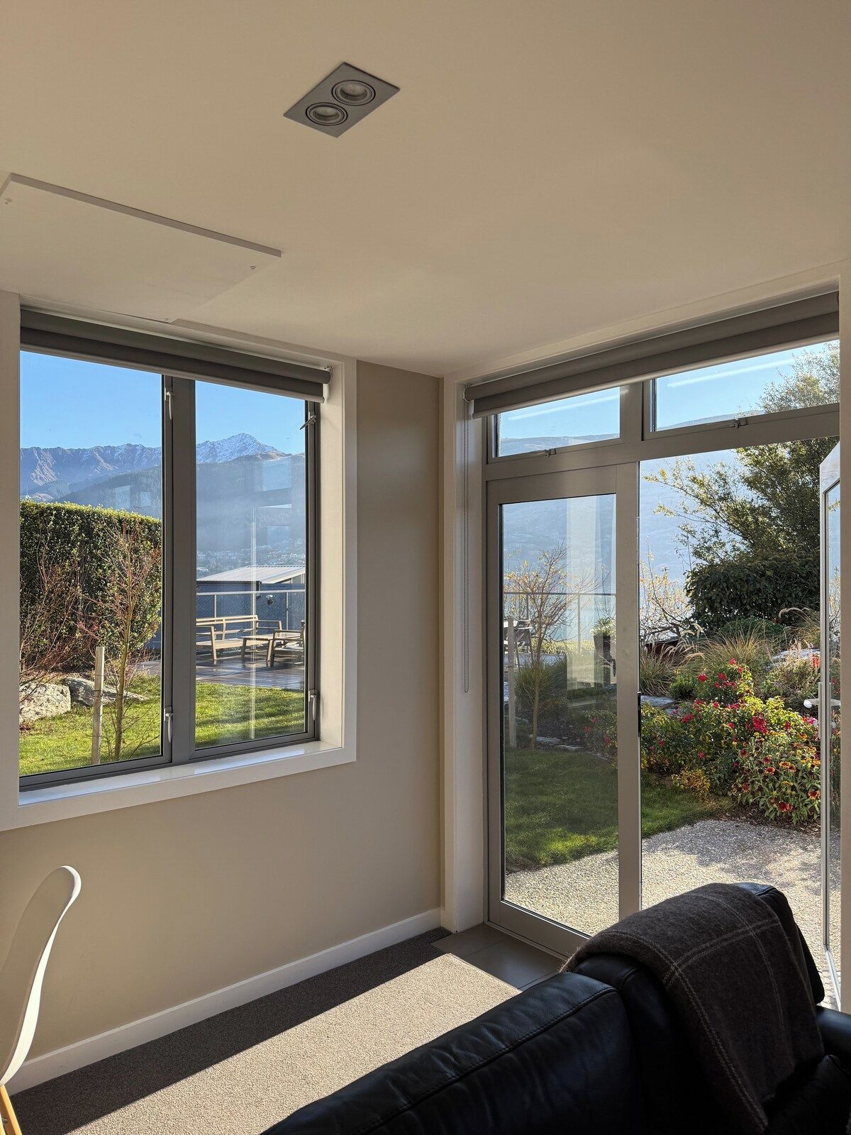 A room with large windows, a black leather sofa, and a view of a garden and mountains.