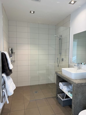 A modern bathroom with white tiles, a shower, a sink, and a mirror.