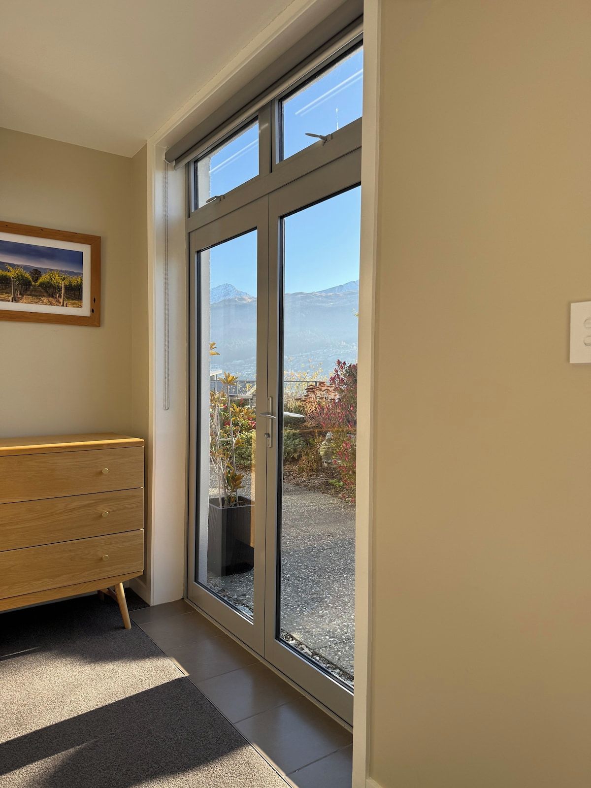 Et værelse med en skydedør, der fører til en balkon med udsigt over bjerge og en have.