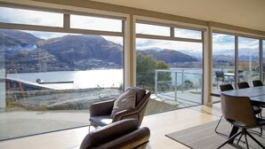 A modern room with large windows offering a view of a lake and mountains. - Alpine Lake Home Summ (Kawarau Falls)