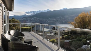A balcony with wicker chairs, a glass railing, and a view of mountains and a lake. - Alpine Lake Home Summ (Kawarau Falls)