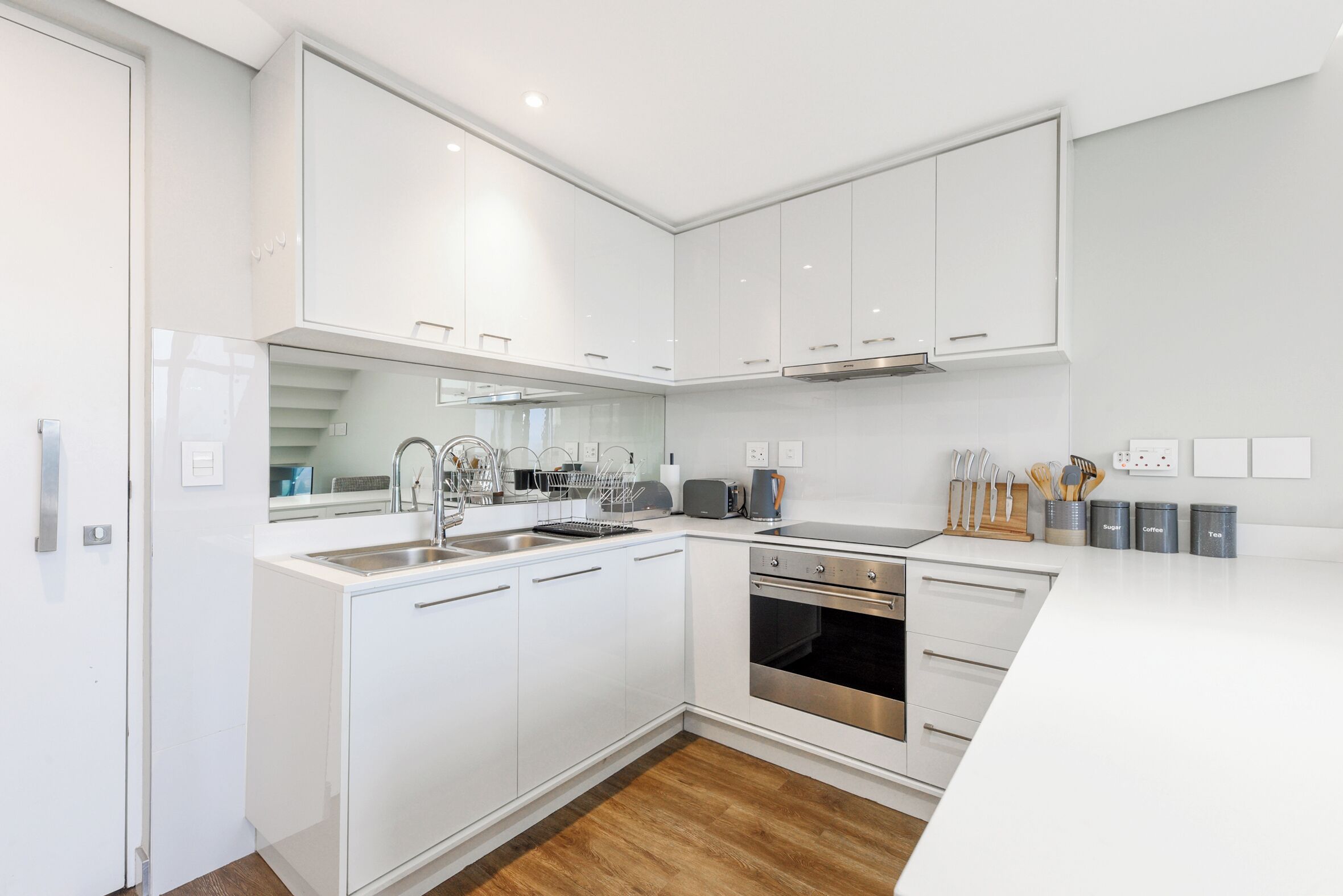 Una cocina moderna con armarios blancos, electrodomésticos de acero inoxidable y piso de madera.