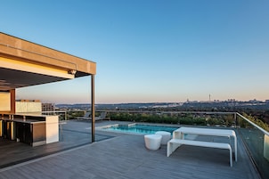 A rooftop terrace with a swimming pool, lounge chairs, and a city view.