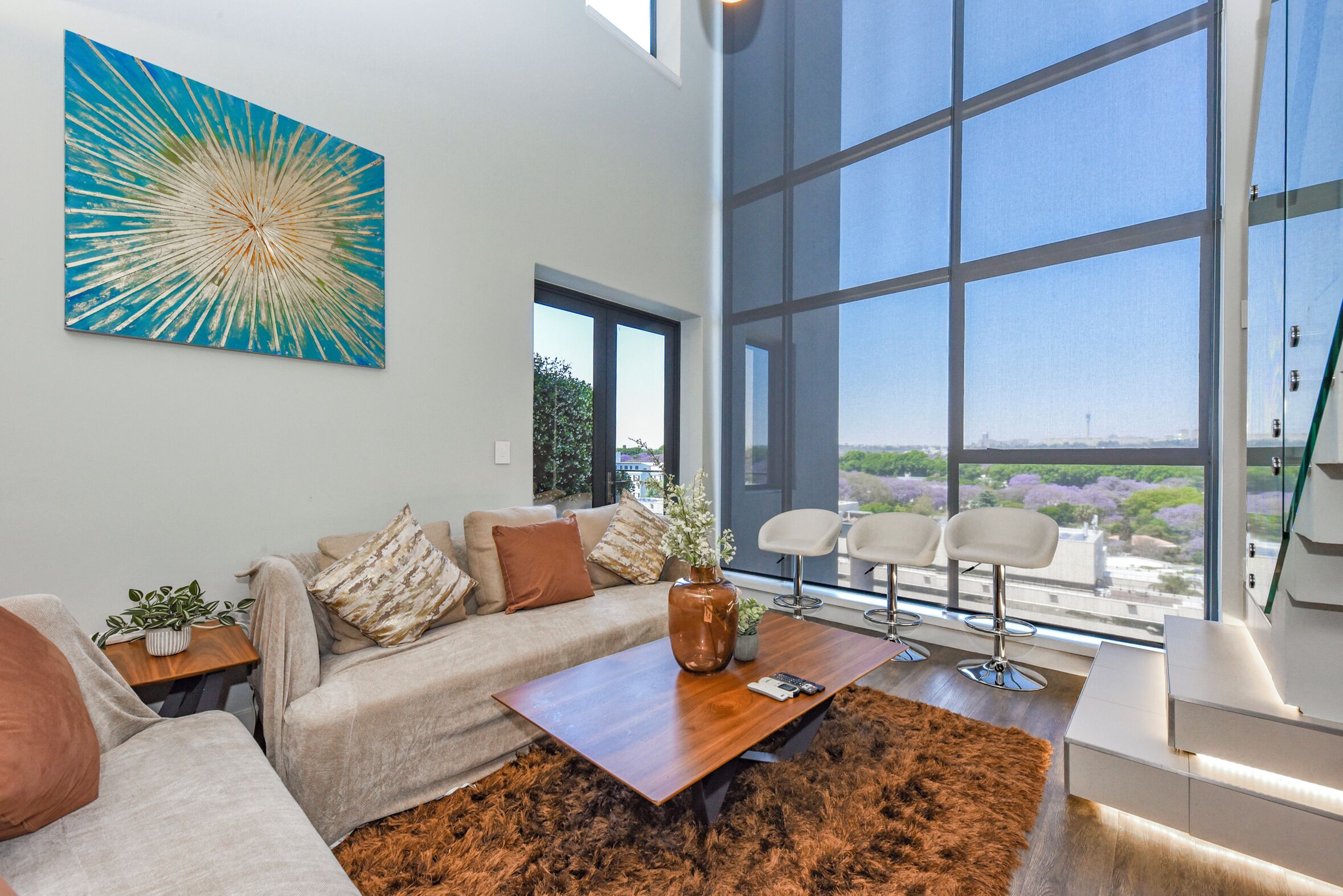 A modern living room with a large window, a sofa, a coffee table, and a painting.