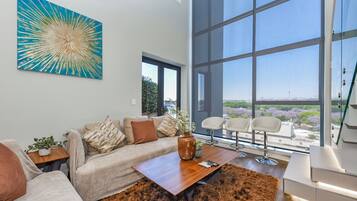 A modern living room with a large window, a sofa, a coffee table, and a painting.
