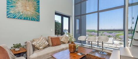 A modern living room with a large window, a sofa, a coffee table, and a painting.
