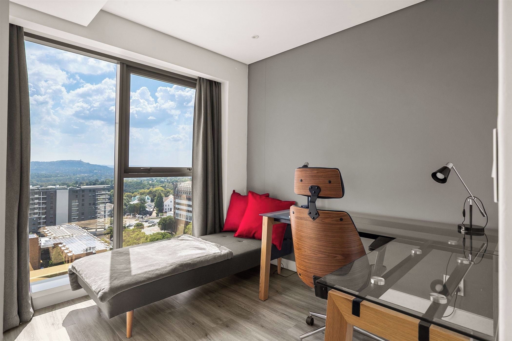 Una camera moderna con un letto, una scrivania, una sedia e un'ampia finestra con vista sulla città.