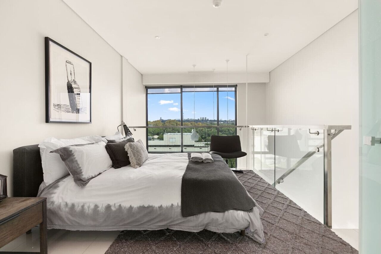 A modern bedroom with a large bed, a view of the city, and a balcony with a chair.