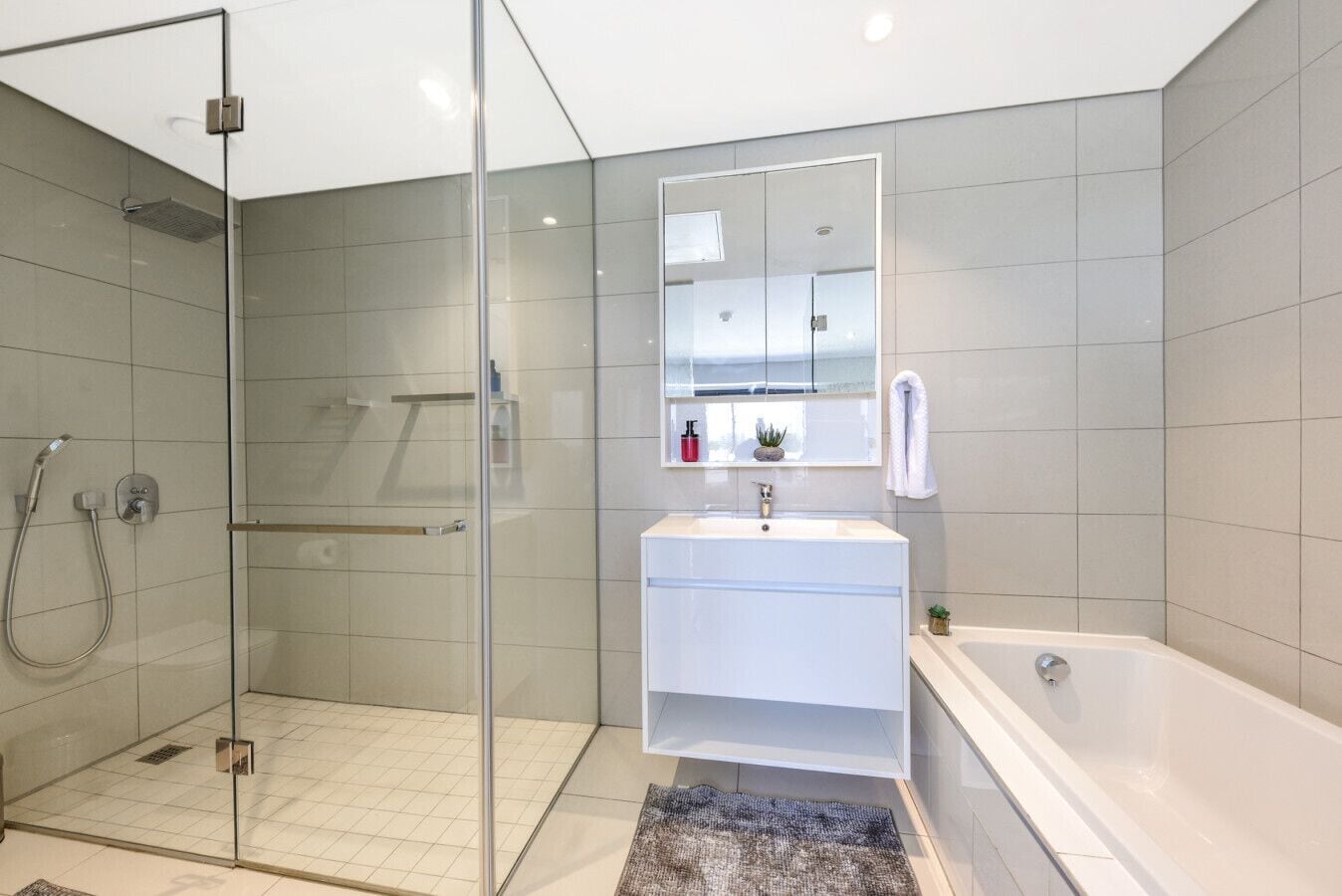 Une salle de bain moderne avec une douche à parois de verre, un lavabo blanc, un miroir et une baignoire.