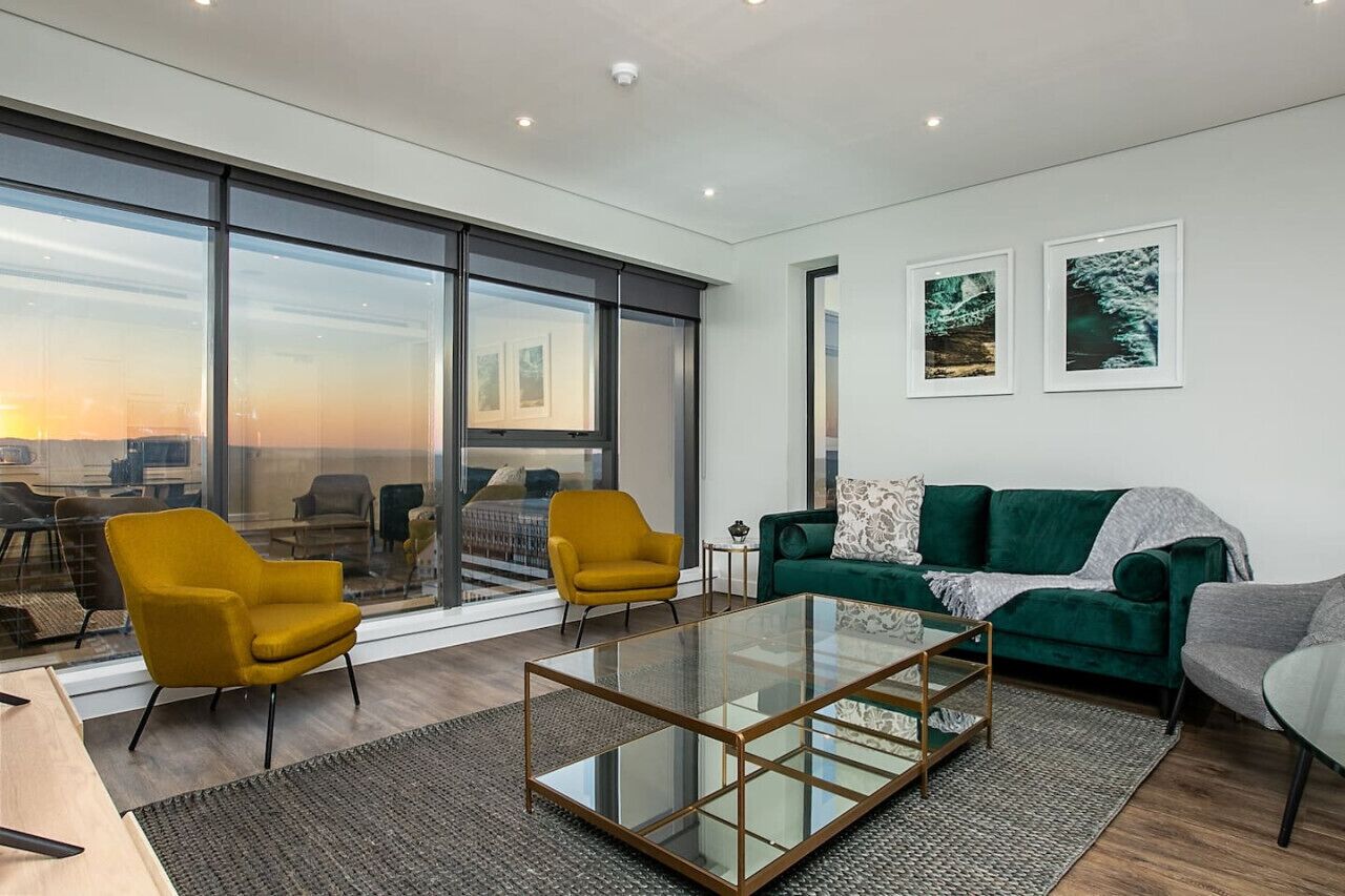 Una sala moderna con una mesa de centro de vidrio, un sofá verde y sillones amarillos.
