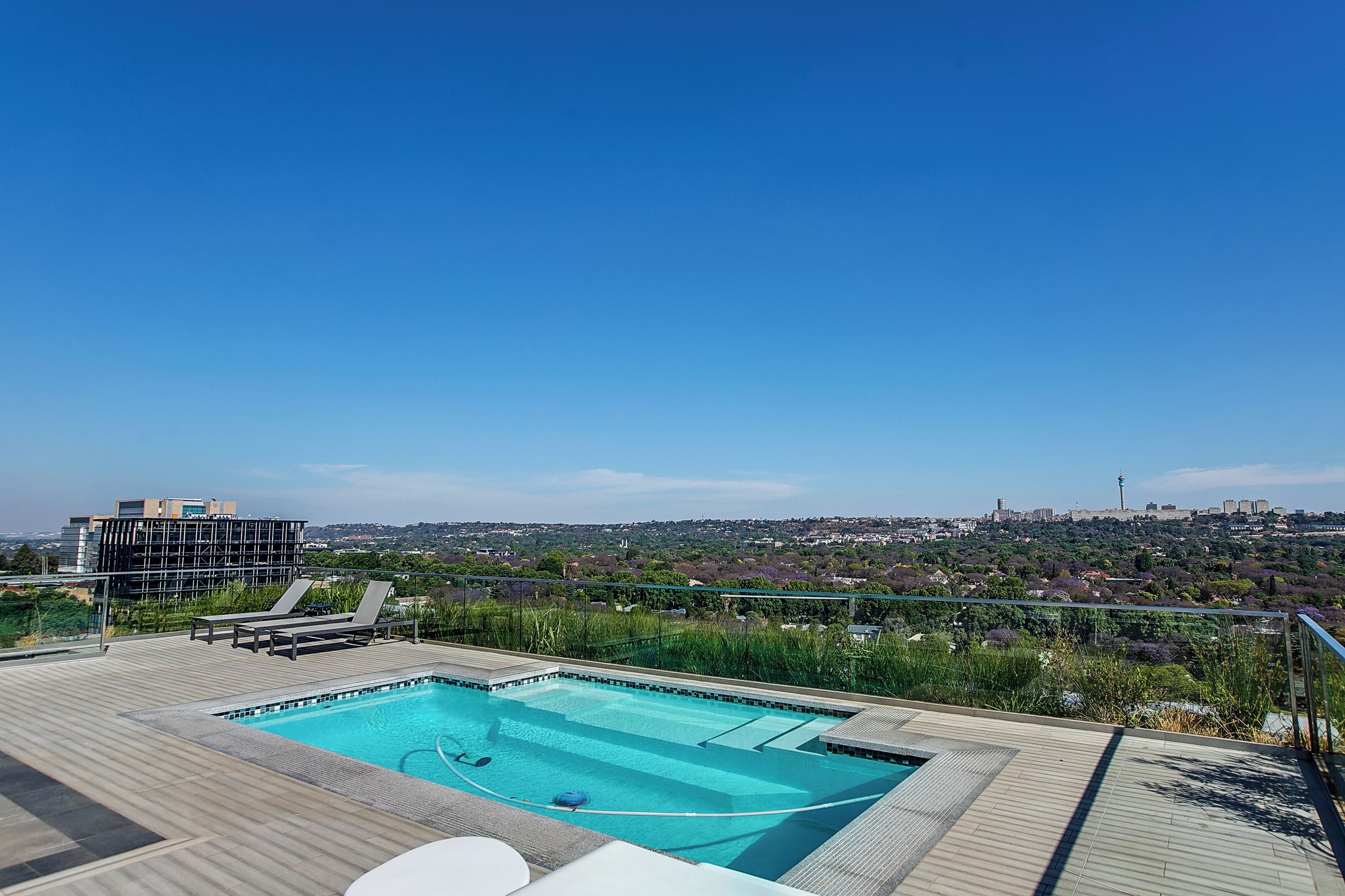 Piscina en la azotea con sillas de descanso y vistas a la ciudad.