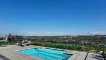Piscina en la azotea con sillas de descanso y vistas a la ciudad.
