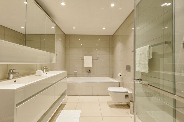 A modern bathroom with a bathtub, toilet, and a glass shower enclosure. - Park Central Residence (Johannesburg)