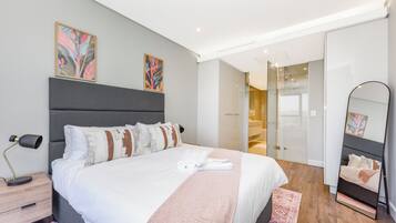 A modern hotel room with a large bed, a bedside table, a lamp, and a mirror.