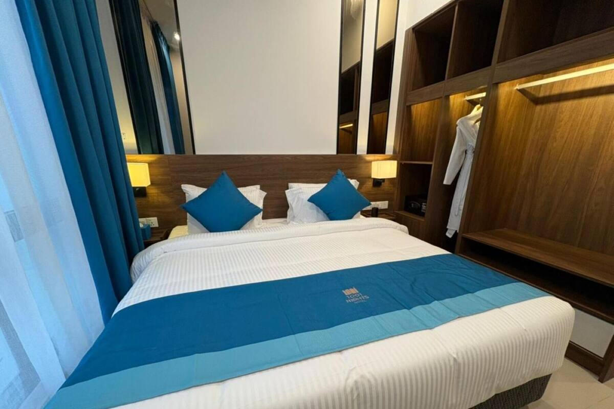A hotel room with a large bed, two pillows, a nightstand, a wooden wardrobe, and a blue-striped bedspread.