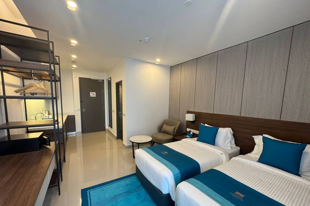 A hotel room with two beds, a desk, a chair, and a small table.