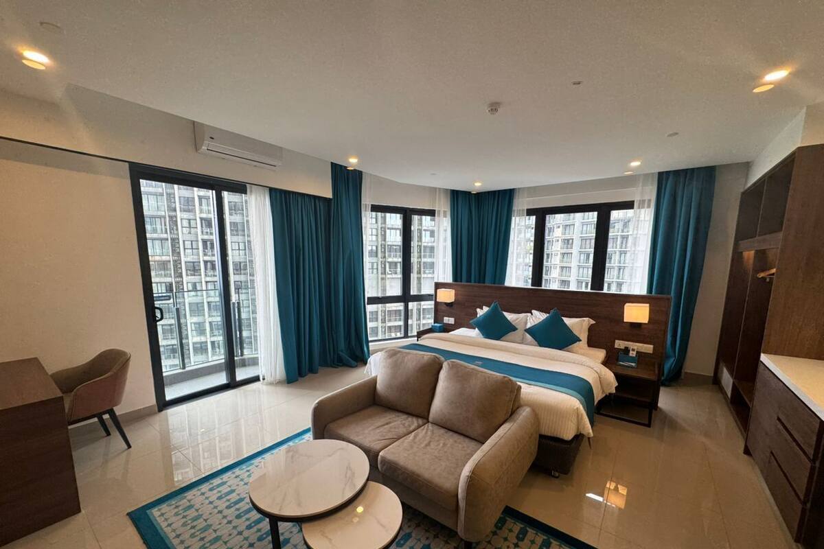 A modern hotel room with a large bed, a sofa, a small table, and a desk.