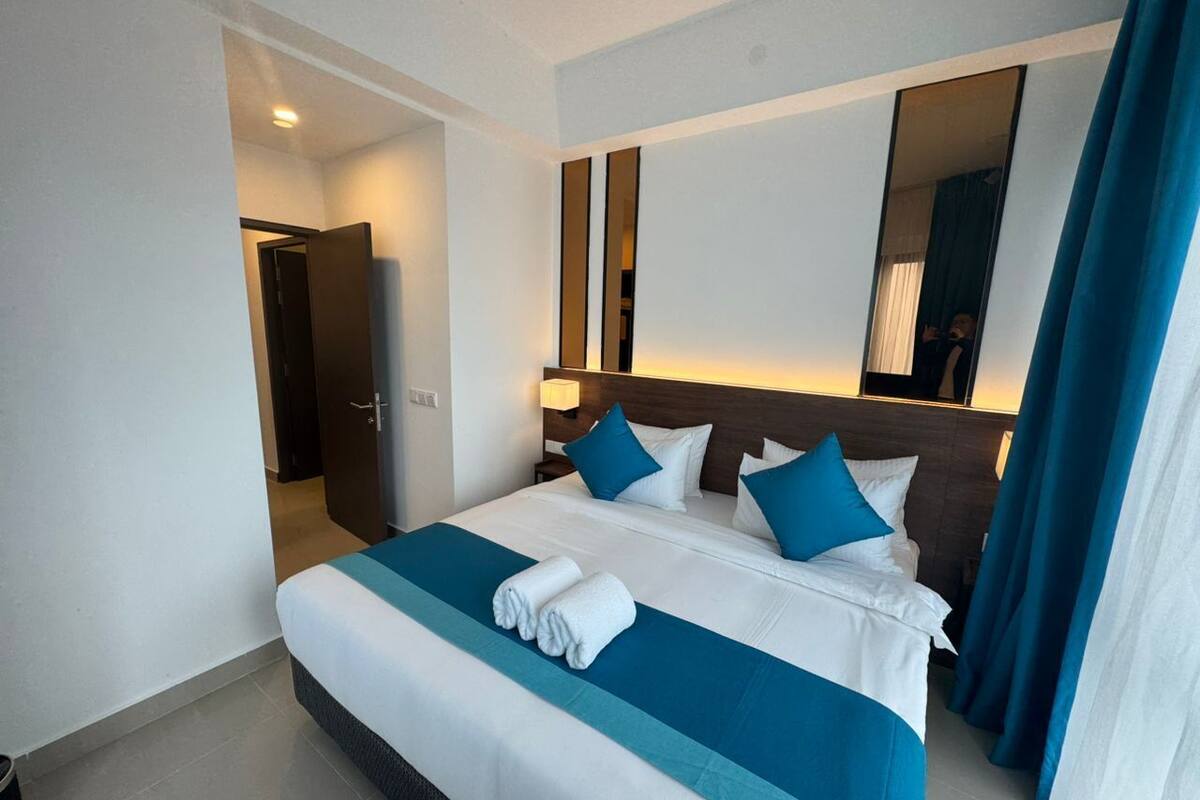 A hotel room with a large bed, a nightstand, a mirror, and a door leading to another room.