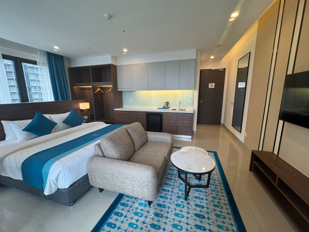 Een hotelkamer met een bed, bank, klein tafeltje en een kitchenette.
